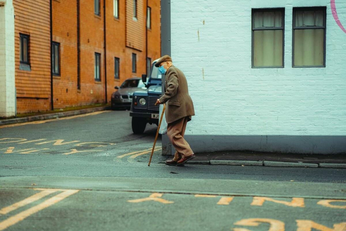 Senior man with cane walking past brick building on urban sidewalk.